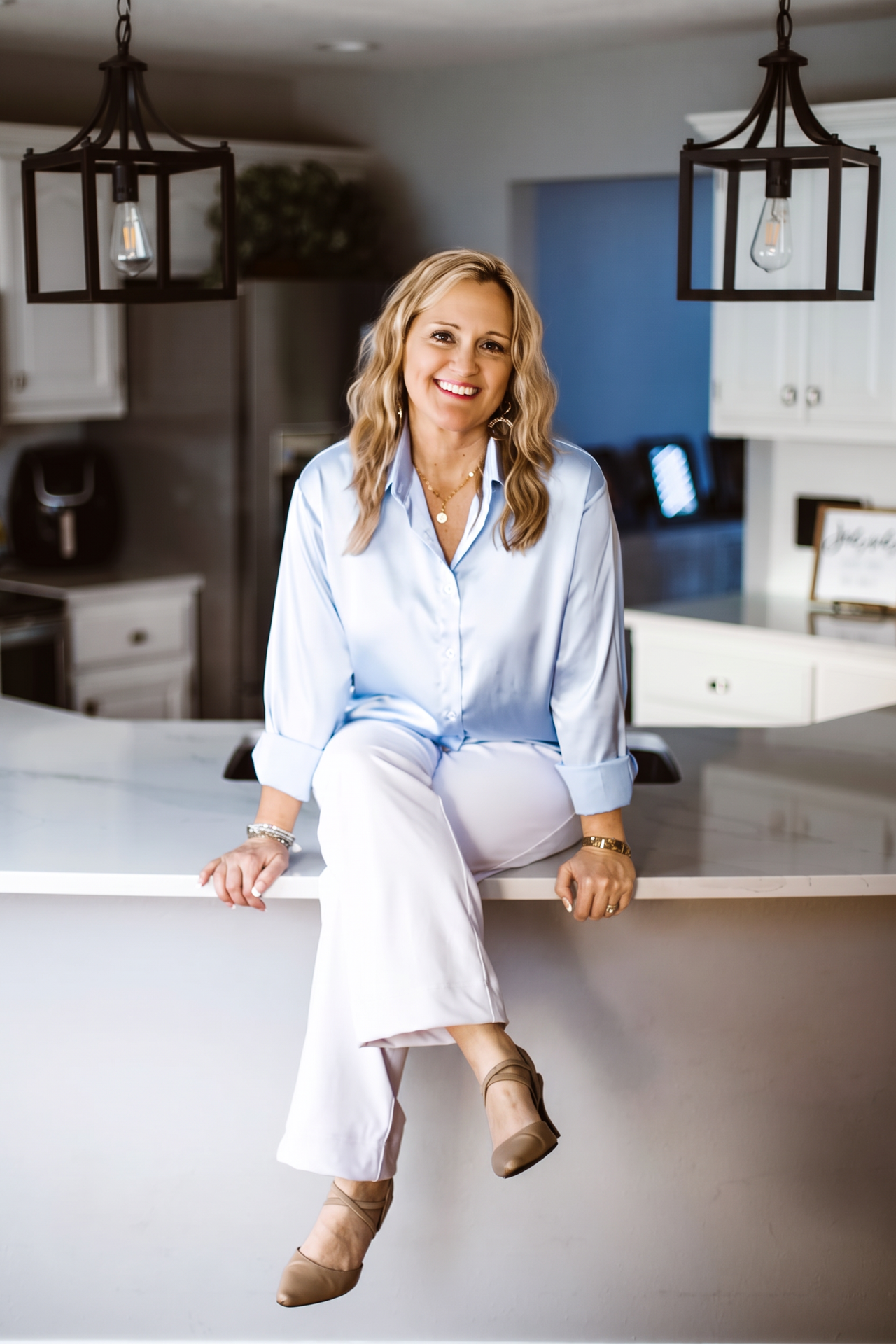 Shanna D. Olds smiling while sitting on a white kitchen counter in soft light